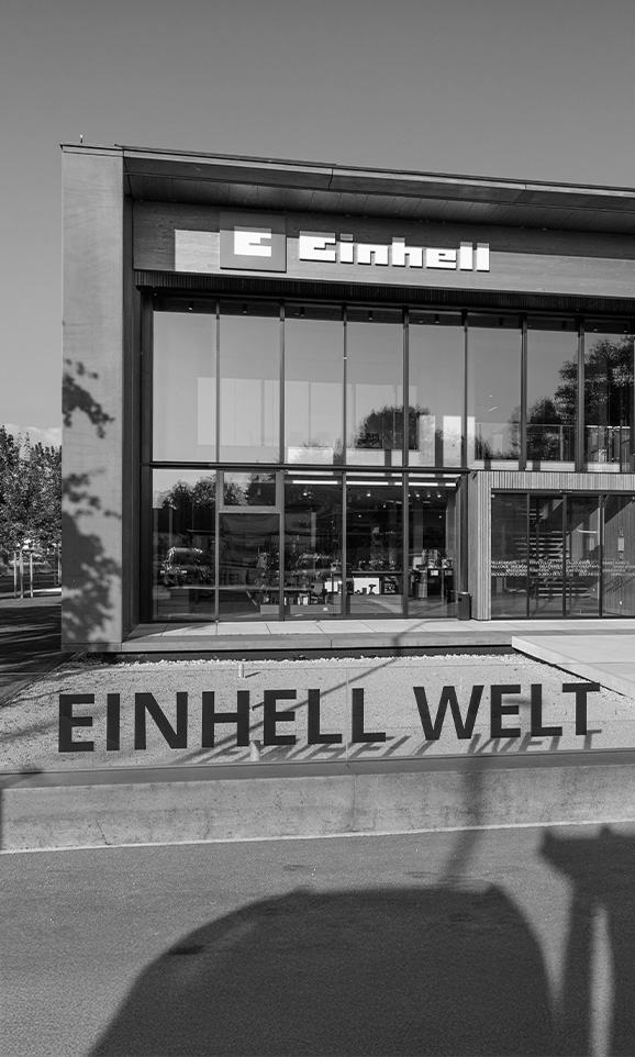 Black-and-white photo of the modern Einhell building with large glass front and the sign “Einhell Welt” in the foreground.