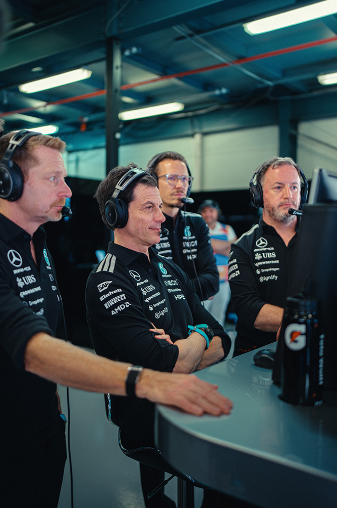 Miembros del equipo de Fórmula 1 con auriculares supervisando la carrera desde el muro de boxes.