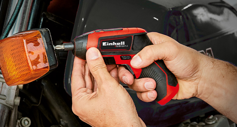 A person uses a cordless screwdriver to fasten a screw to a turn signal.