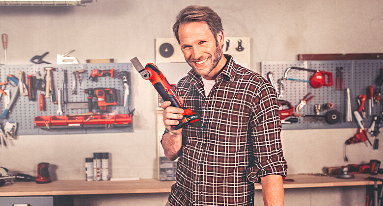 A man standing in his workshop and holding a cordless multifunctional tool from Einhell in his hand.